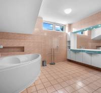 A bathroom in a villa with a corner bathtub, mirror, and cabinets, tiled.