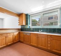 A kitchen in a villa with wooden cabinets and green tiles, open space to the living room.