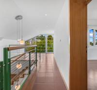 Interior of a villa with a glass wall and a circular window, staircase, and lighting fixtures.