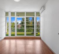 A white room with a wooden floor and glass doors overlooking greenery in a villa.