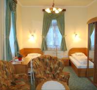 A room in a hotel and guesthouse with beds, chairs, a mirrored wardrobe, and decorative curtains.