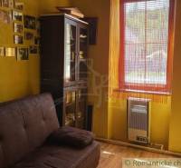 Yellow room in a family house with a sofa, display cabinet, and photos on the wall.