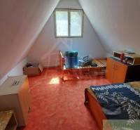 An attic room in a cottage with simple furnishings, an orange carpet, and a bed.