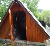 A wooden cellar at a family house in the city of FONY, surrounded by greenery and a fence.