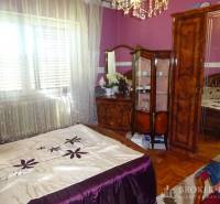 A bedroom in a family house with wooden furniture, purple walls, and decorative curtains.