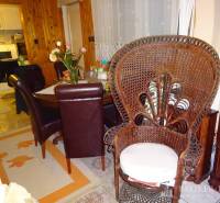 Dining room in a family house with a wicker chair, flowers, and wooden furniture near the kitchen.