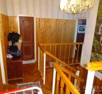 A hallway in a family house with wooden paneling, railing, and stairs, with a painting on the wall.