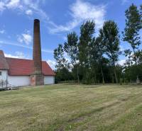 Old brick chimney next to a building in Zemianske Sady, warehouses and halls, surrounded by trees.