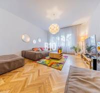 Living room in a two-room apartment with a sofa, wooden floor, and colorful rug.