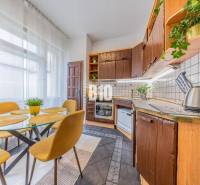 A kitchen in a 2-room apartment with a wooden kitchen unit, a dining table, and light curtains.