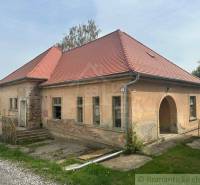 An older family house in Rimavská Sobota, with peeling plaster, a red roof, in a rural setting.