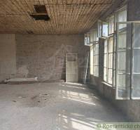 A spacious room with tall windows and a worn-out ceiling in a family house.