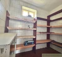 A pantry in a family house with shelves, tiled walls, a small window letting in light.
