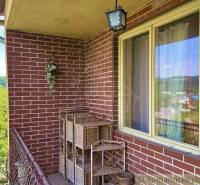 A brick balcony of a family house in Gemerská Hôrka with hanging flowers and a view.