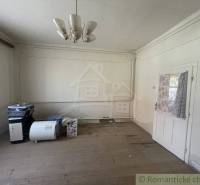 A room in a family house with a wooden floor, a chandelier, and white walls.