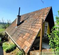 A cottage in Malé Kozmálovce with a steep roof and green surroundings, rural environment.