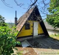 Yellow cottage in Malé Kozmálovce with a triangular roof, surrounded by greenery.