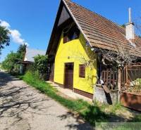 The yellow cottage in Malé Kozmálovce with a clay roof, surrounded by greenery and an access road.