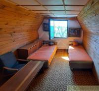 Wooden paneling, two beds, an armchair, and a table in an attic room in a cottage.