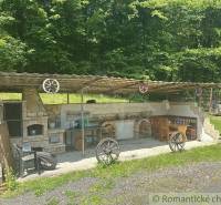 Covered garden seating area at a family house in Poltár with a stone fireplace and wooden decorations.