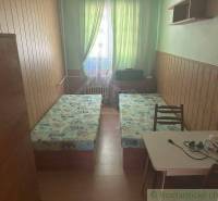 A room in a family house with two beds, a table, and green curtains.