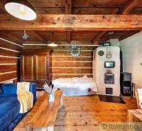 A wooden cabin with a stove, wooden furniture, a sofa, and a bed in a cozy interior.