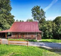 A cottage in nature near Kežmarok with a wooden fence and trees in the background.