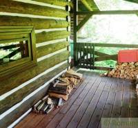 Wooden porch of the cottage in Kežmarok with stored firewood and a view of the greenery.