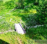 A wooden bridge on a meadow near a cottage in Kežmarok, surrounded by greenery and flowers.