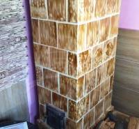 A tiled stove in a cabin with wooden details and a table in a cozy corner.