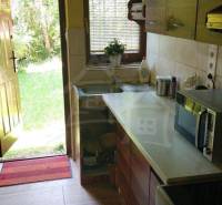 A kitchen in a cottage with a garden view, featuring wooden furniture and ceramic tiles.