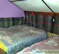 Two beds in the attic of the cottage with colorful textiles on the walls.