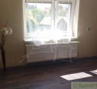 A room with a large window, wooden floor, and floral decoration in a family house.