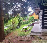 A family house in Ružomberok with wooden walls, a bench, and a garden surrounded by trees.