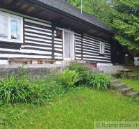 A family house in Ružomberok offers a wooden facade surrounded by greenery and wooden furniture.