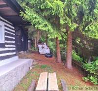 A traditional wooden family house near the forest in Ružomberok, spruce trees, and a wooden fence.