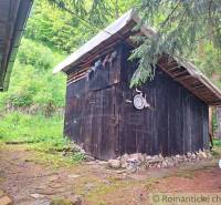 A wooden shelter in the garden of a family house in Ružomberok, surrounded by greenery and trees.