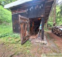 A shed by a family house in Ružomberok, surrounded by shelters and wood in a forest area.