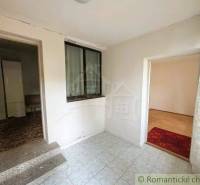 A hallway of a family house with tiles, carpet, and a view into two rooms.