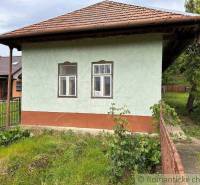 A cottage in Nové Zámky with a green facade and a sloped roof, surrounded by greenery.