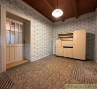 The interior of a cabin with a wooden ceiling, floral wallpaper, and vintage furniture.