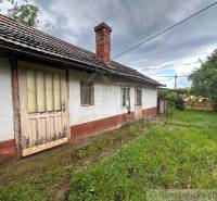 An older cottage in Nové Zámky with wooden doors and a grassy yard.
