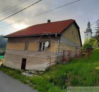 A family house in Žiar nad Hronom with a church in the background, green meadow, road.
