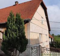 A family house in Žiar nad Hronom with a red roof, next to it is a conifer and a fence.