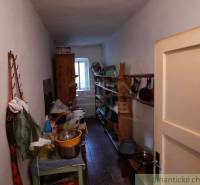 A narrow room with old furniture and shelves in a family house, with a door at the front.