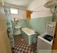 A bathroom in a family house with a bathtub, washing machine, and green tiles.
