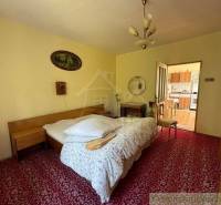 A bedroom with a bed, a mirror, and open doors leading to the kitchen in a family house.