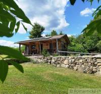 A wooden cottage in Veľký Krtíš surrounded by greenery and a stone wall.