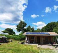 A cottage in Veľký Krtíš with a lawn and solar panels, surrounded by greenery and a blue sky.