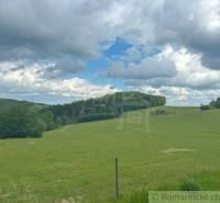 Green meadows and hills under a cloudy blue sky in the Gardens in České Brezové.
